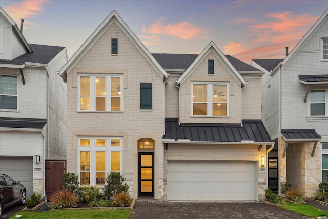 view of front facade with a standing seam roof, a garage, decorative driveway, brick siding, and metal roof