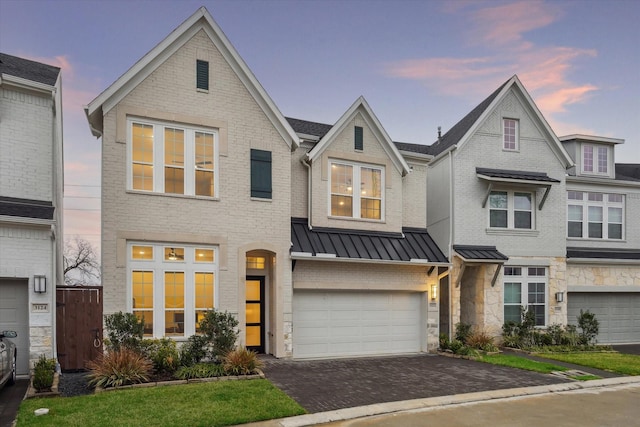 view of front of property featuring brick siding, metal roof, decorative driveway, an attached garage, and a standing seam roof