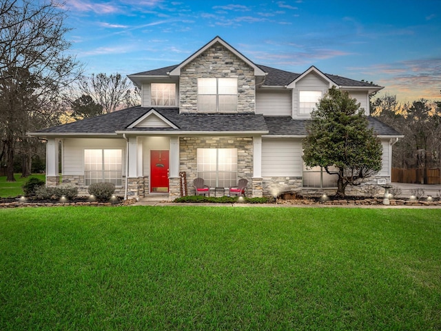 view of front of house featuring entry steps, roof with shingles, a lawn, and stone siding