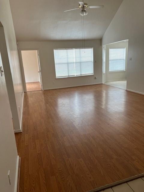 unfurnished room featuring vaulted ceiling, baseboards, a ceiling fan, and wood finished floors