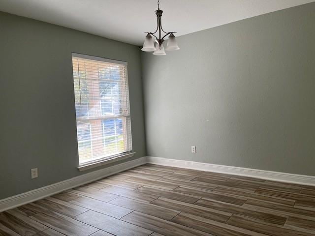 unfurnished room with wood finish floors, a healthy amount of sunlight, and an inviting chandelier