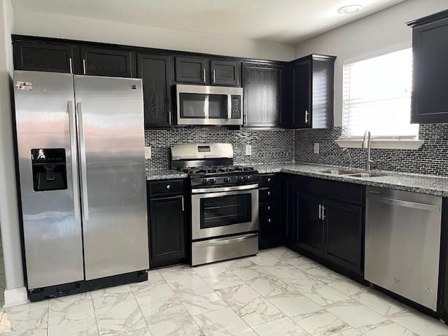 kitchen with dark cabinets, light stone counters, marble finish floor, and appliances with stainless steel finishes