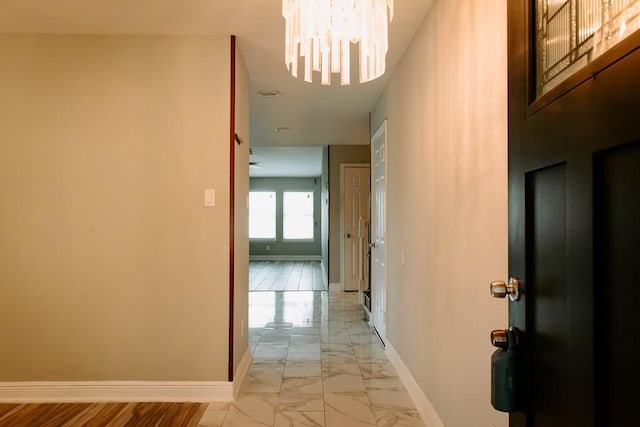 hall featuring marble finish floor, baseboards, and an inviting chandelier