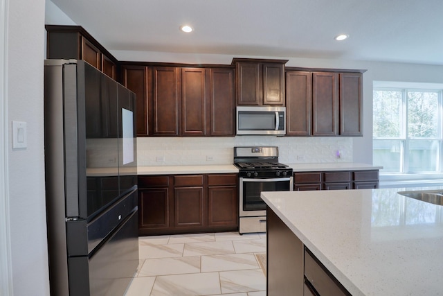 15158 N Heron Heights Way, Magnolia, TX 77354 - kitchen with dark brown cabinets, appliances with stainless steel finishes, light stone counters, recessed lighting, and tasteful backsplash