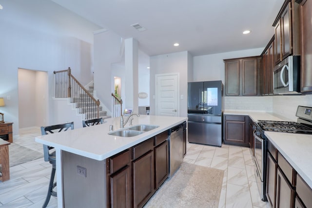 15158 N Heron Heights Way, Magnolia, TX 77354 - kitchen featuring dark brown cabinets, appliances with stainless steel finishes, a sink, an island with sink, and a kitchen bar