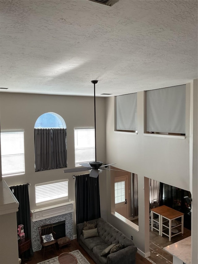 living room featuring wood-type flooring, a tiled fireplace, ceiling fan, and a textured ceiling