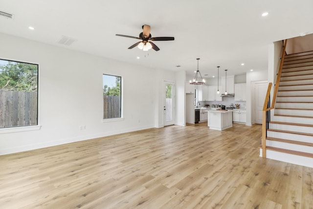 unfurnished living room featuring a healthy amount of sunlight, ceiling fan with notable chandelier, and light hardwood / wood-style flooring