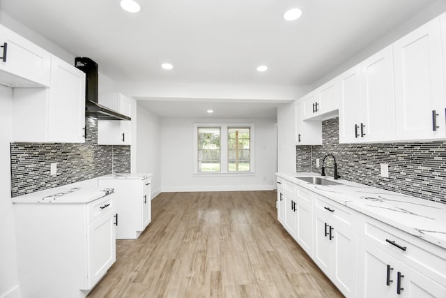 kitchen with wall chimney exhaust hood, light stone counters, a sink, and white cabinets