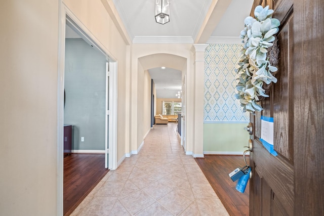 hallway featuring light wood-type flooring, baseboards, arched walkways, and ornamental molding