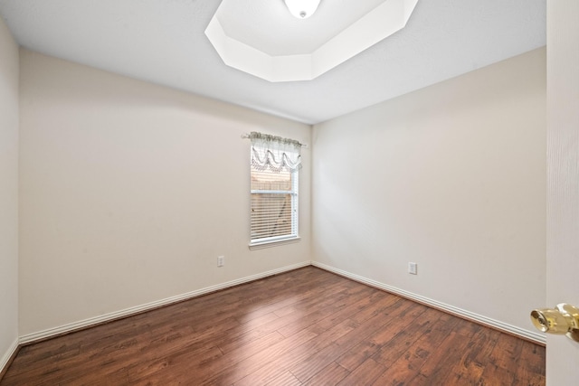 empty room featuring dark wood-style floors, baseboards, and a tray ceiling