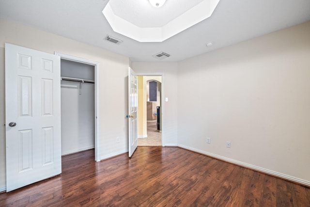 unfurnished bedroom featuring baseboards, visible vents, a raised ceiling, and dark wood-style flooring