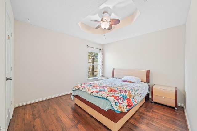 bedroom with dark wood-type flooring, a raised ceiling, and baseboards