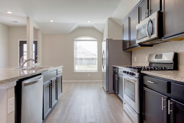 kitchen with tasteful backsplash, appliances with stainless steel finishes, vaulted ceiling, a sink, and dark brown cabinets