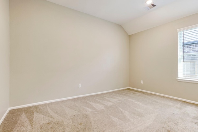 spare room featuring lofted ceiling, light colored carpet, visible vents, and baseboards