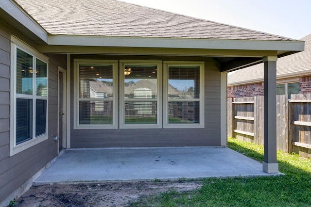 property entrance with a shingled roof, a patio area, and fence