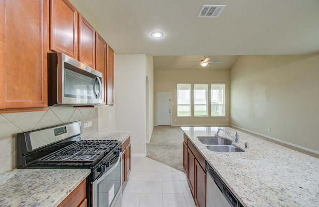 kitchen with sink, appliances with stainless steel finishes, light stone counters, tasteful backsplash, and light colored carpet