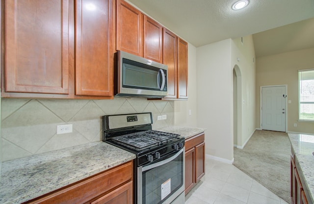 kitchen featuring stainless steel appliances, light carpet, light stone counters, and decorative backsplash