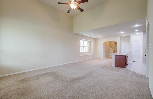 unfurnished living room with ceiling fan, light colored carpet, sink, and a high ceiling