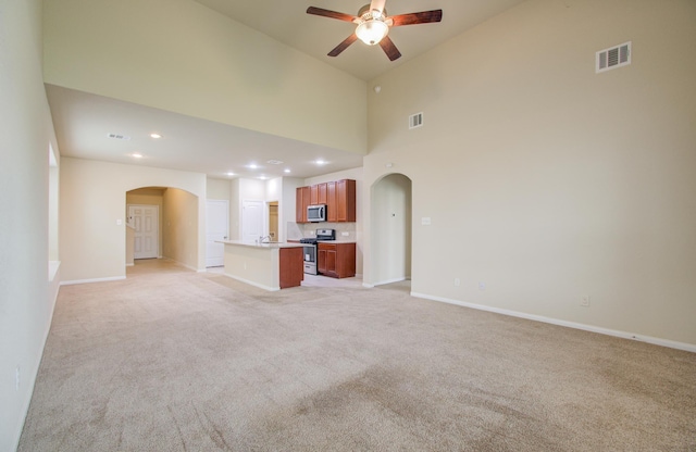 unfurnished living room featuring ceiling fan, light colored carpet, and a towering ceiling