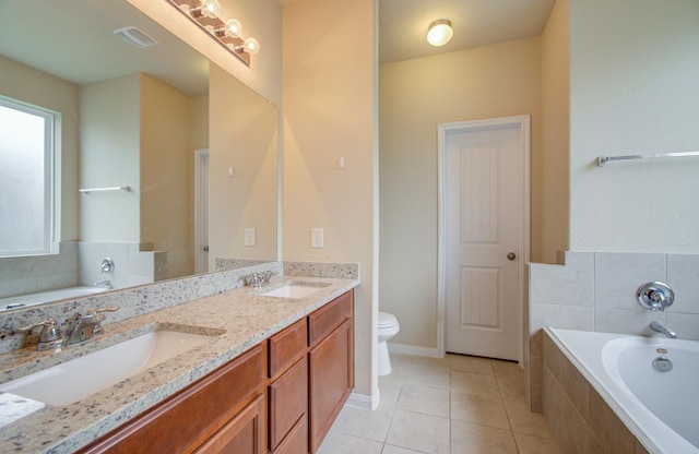 bathroom with tile patterned flooring, vanity, tiled tub, and toilet