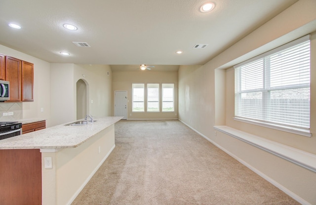 kitchen featuring sink, ceiling fan, tasteful backsplash, an island with sink, and light carpet