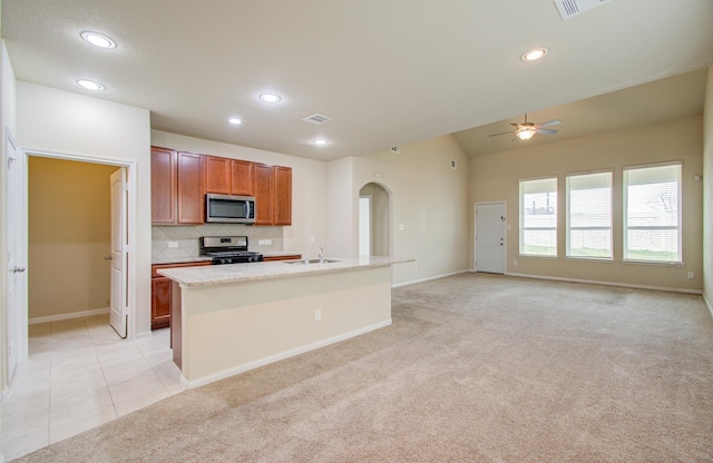 kitchen with sink, appliances with stainless steel finishes, tasteful backsplash, an island with sink, and light carpet