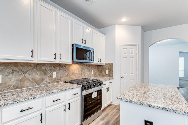 kitchen with white cabinetry, stainless steel appliances, a center island, light stone countertops, and decorative backsplash