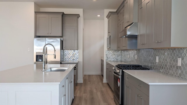 kitchen featuring appliances with stainless steel finishes, wood-type flooring, sink, gray cabinetry, and backsplash