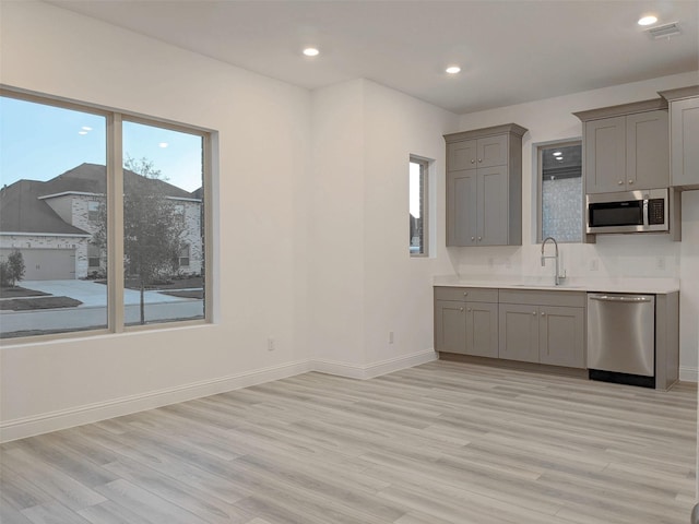 kitchen featuring stainless steel appliances, sink, light hardwood / wood-style flooring, and gray cabinets