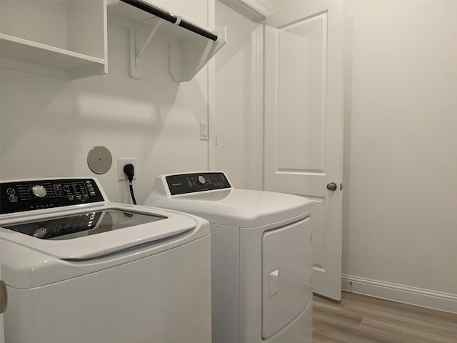 laundry area with washing machine and clothes dryer and light wood-type flooring