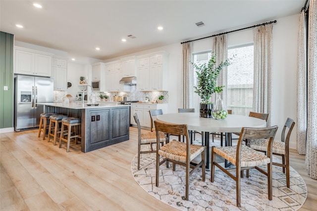 kitchen with backsplash, white cabinets, a kitchen breakfast bar, stainless steel refrigerator with ice dispenser, and a center island with sink