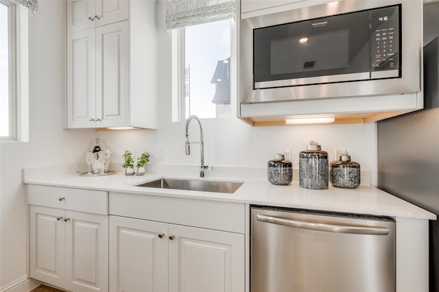 kitchen featuring built in microwave, sink, stainless steel dishwasher, and white cabinets