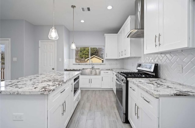 kitchen with wall chimney range hood, hanging light fixtures, white cabinets, and appliances with stainless steel finishes