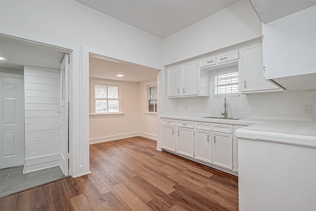 kitchen with light wood finished floors, tasteful backsplash, tile countertops, white cabinetry, and a sink