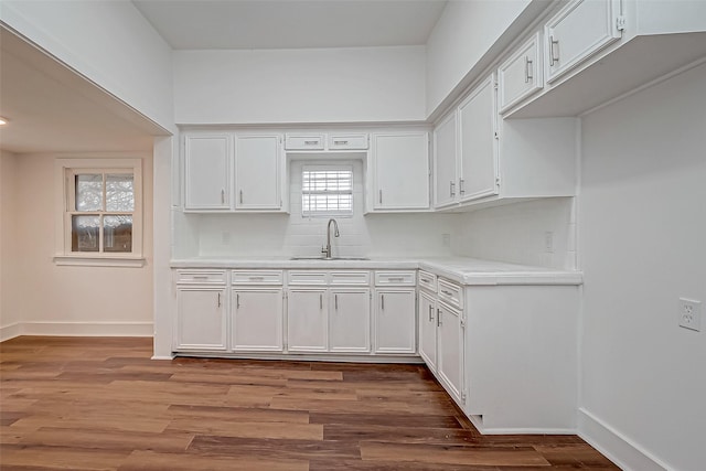 kitchen with light countertops, white cabinets, a sink, wood finished floors, and baseboards