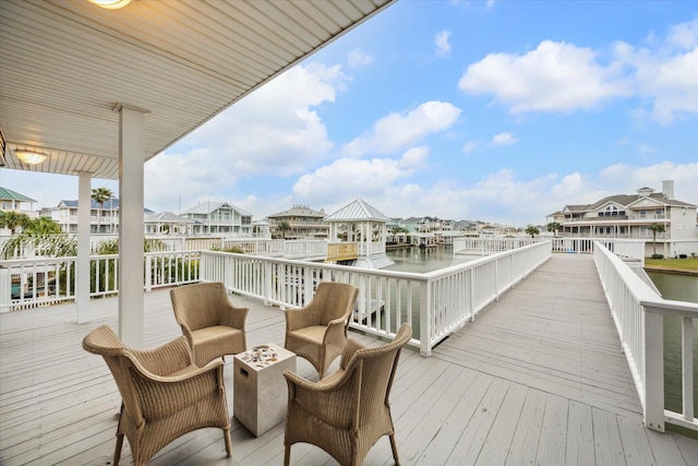 wooden terrace featuring a water view, an outdoor living space with a fire pit, and a residential view