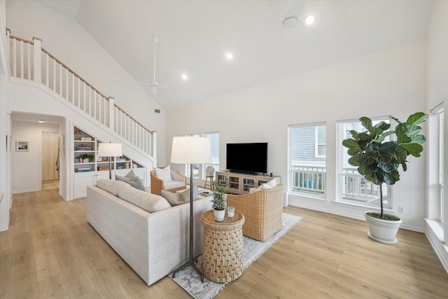 living room featuring recessed lighting, light wood-style floors, high vaulted ceiling, baseboards, and stairs