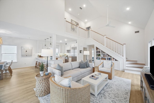 living room with stairs, high vaulted ceiling, light wood finished floors, and visible vents