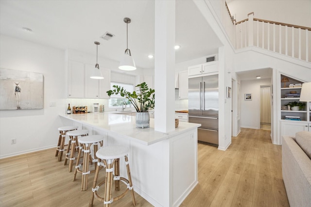 kitchen featuring stainless steel built in fridge, white cabinetry, visible vents, and a breakfast bar