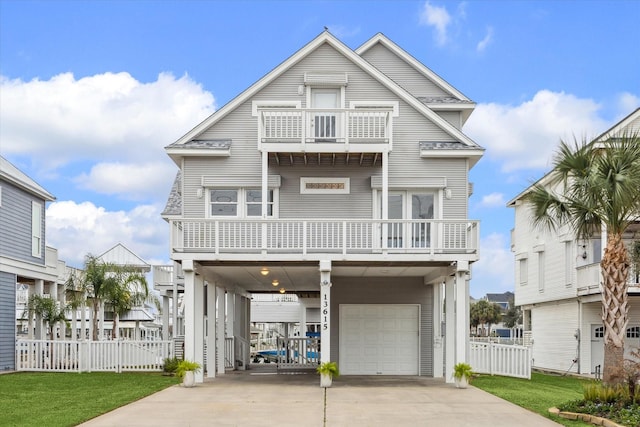 coastal home featuring an attached garage, a balcony, fence, concrete driveway, and a front lawn