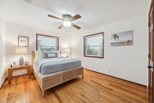 bedroom featuring light wood-style floors, multiple windows, a ceiling fan, and a textured ceiling