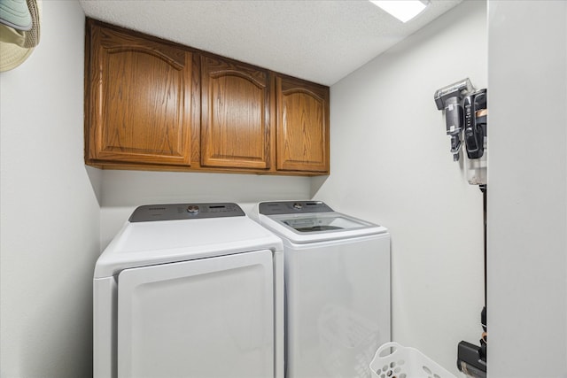 washroom with washer and dryer, cabinet space, and a textured ceiling