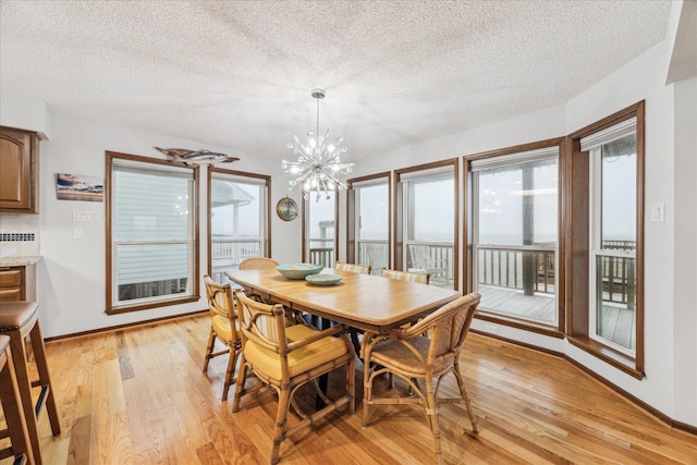 dining area featuring a textured ceiling, baseboards, light wood-style flooring, and a notable chandelier