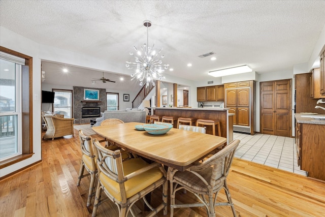 dining area with visible vents, stairway, light wood-style flooring, a large fireplace, and a textured ceiling