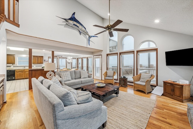 living room featuring light wood finished floors, high vaulted ceiling, a textured ceiling, and ceiling fan with notable chandelier