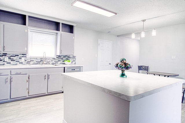 kitchen featuring light hardwood / wood-style flooring, sink, a center island, decorative light fixtures, and tasteful backsplash