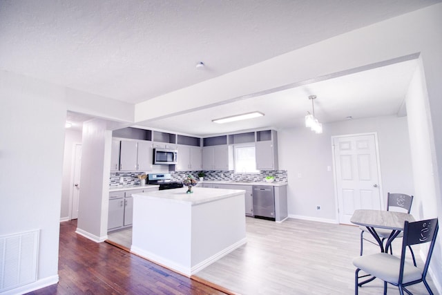 kitchen with appliances with stainless steel finishes, light wood-type flooring, pendant lighting, gray cabinetry, and decorative backsplash