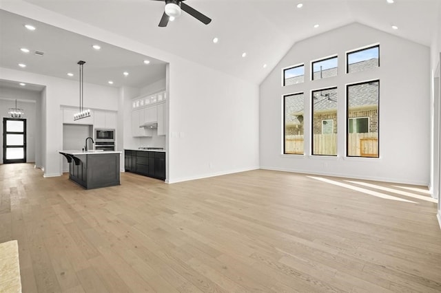 unfurnished living room with ceiling fan with notable chandelier, high vaulted ceiling, light hardwood / wood-style floors, and sink