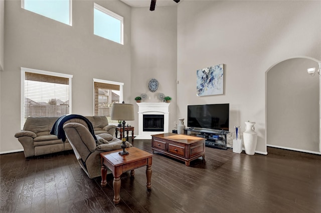 living room with ceiling fan, dark hardwood / wood-style floors, and a towering ceiling