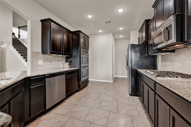 kitchen with stainless steel appliances, dark brown cabinets, tasteful backsplash, light stone counters, and light tile patterned flooring